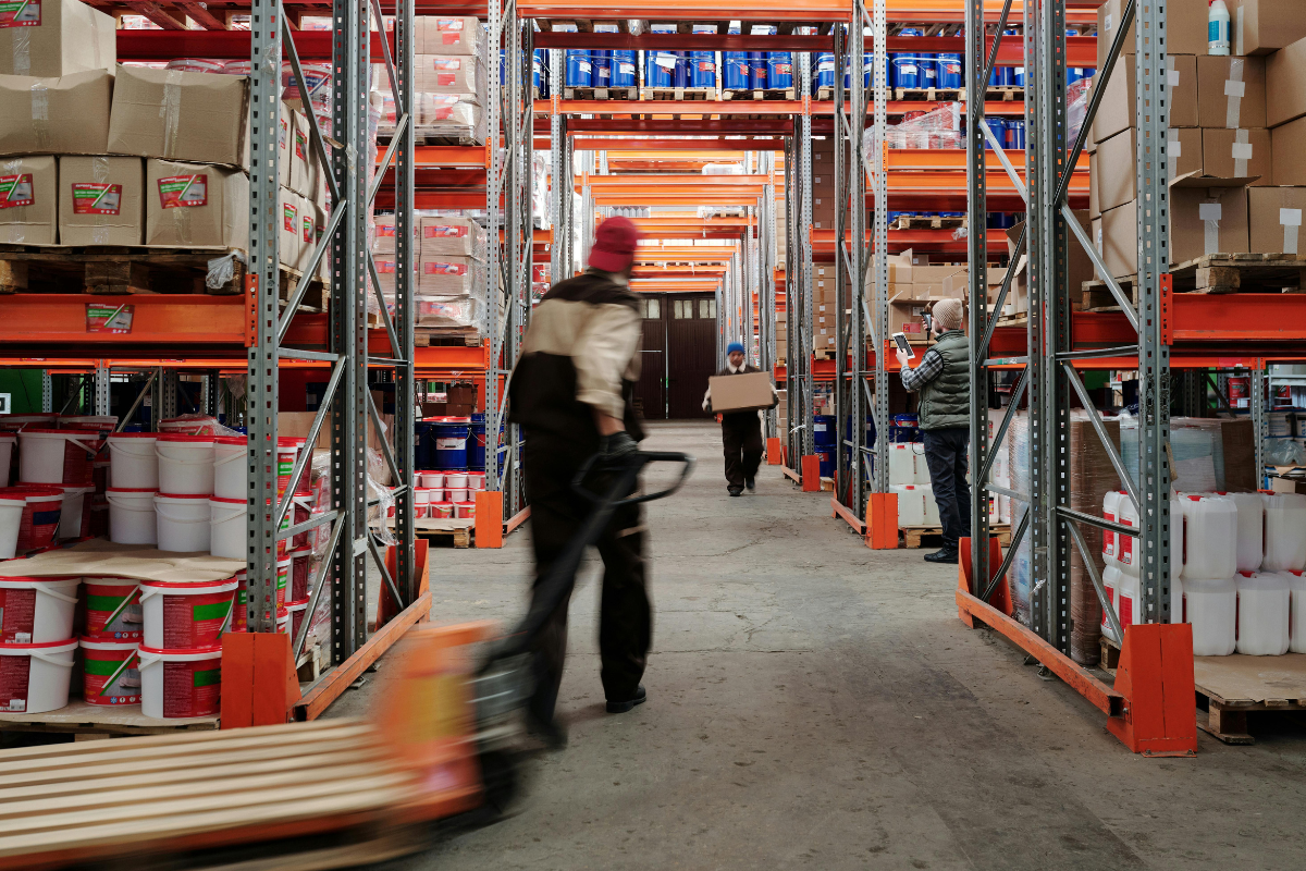 Warehouse aisle with workers moving pallets and boxes between tall industrial storage racks