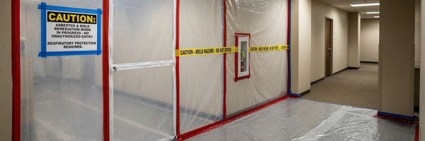 Containment area set up for hazardous material remediation with plastic barriers and caution signage indicating asbestos and mold work in progress