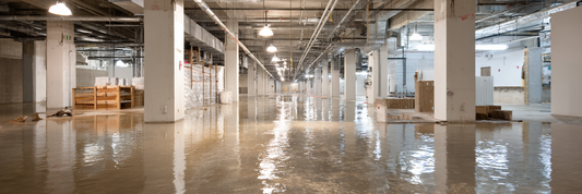 Large commercial basement flooded with standing water across the concrete floor and support columns