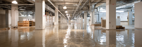 Large commercial basement flooded with standing water across the concrete floor and support columns
