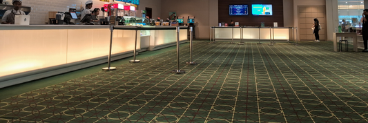 Commercial concession counter area with patterned carpet flooring and queue barriers in a public facility.
